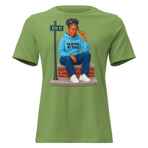 Women's relaxed-fit Enjoying My Peace Tee in leaf green showing a silver-haired woman relaxing on her front stoop, front view