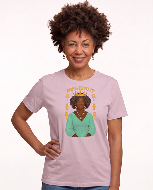 Charmaine, a woman in her 40s with a curly afro and freckles, wearing the Born Into It Tee Forward Gaze in Light Violet with a crowned queen and Ankh symbols. Hands On 5th St.