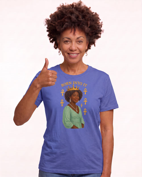 Charmaine, a woman in her 40s with a curly afro and freckles, wearing the Born Into It Tee Reflection in Heather True Royal with a crowned queen and Ankh symbols. Hands On 5th St.