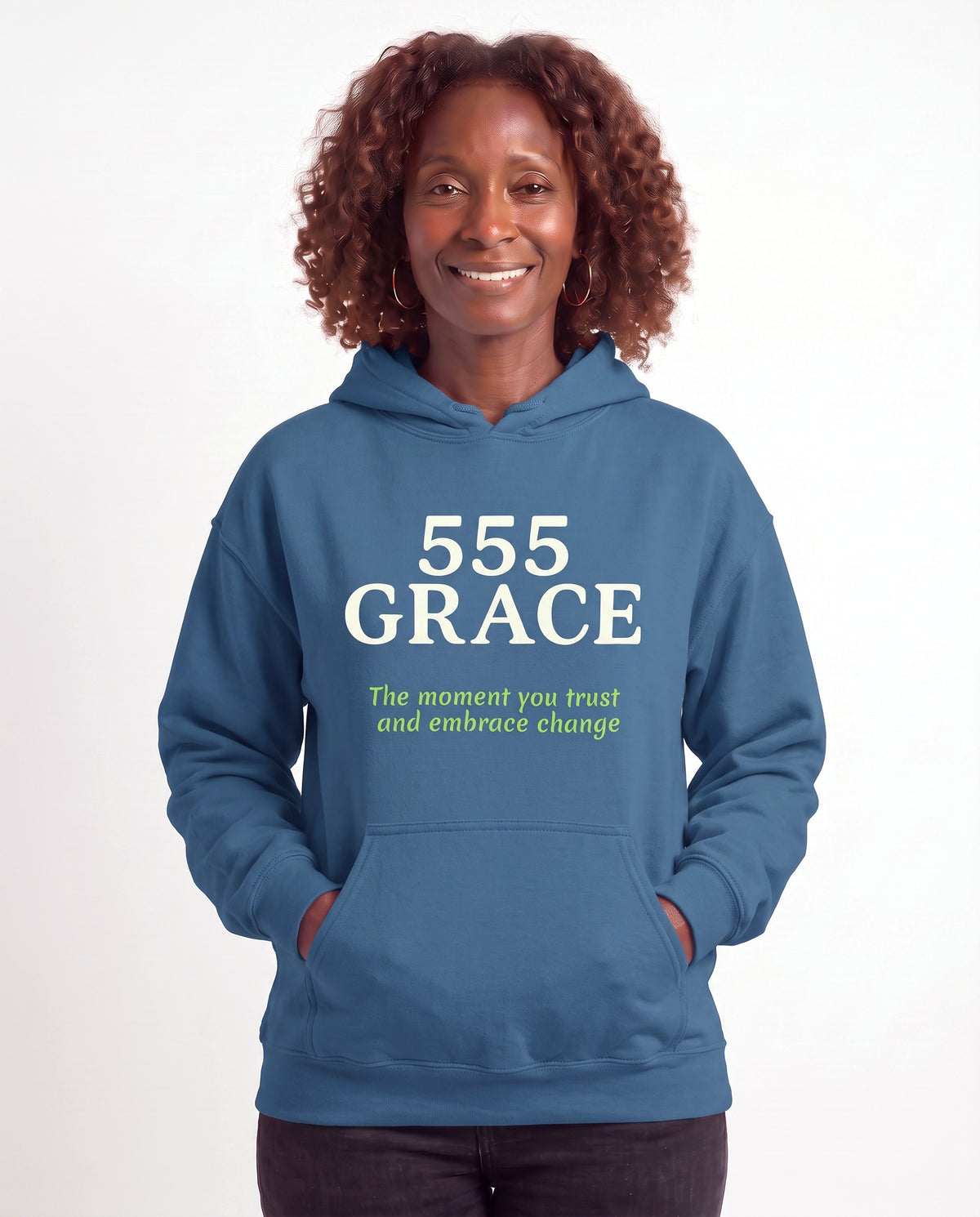 Grace, a Black woman in her 50s with shoulder-length auburn curls and gold hoops, wearing the 555 GRACE Hoodie in Indigo Blue with the words The moment you trust and embrace change. Hands On 5th St.
