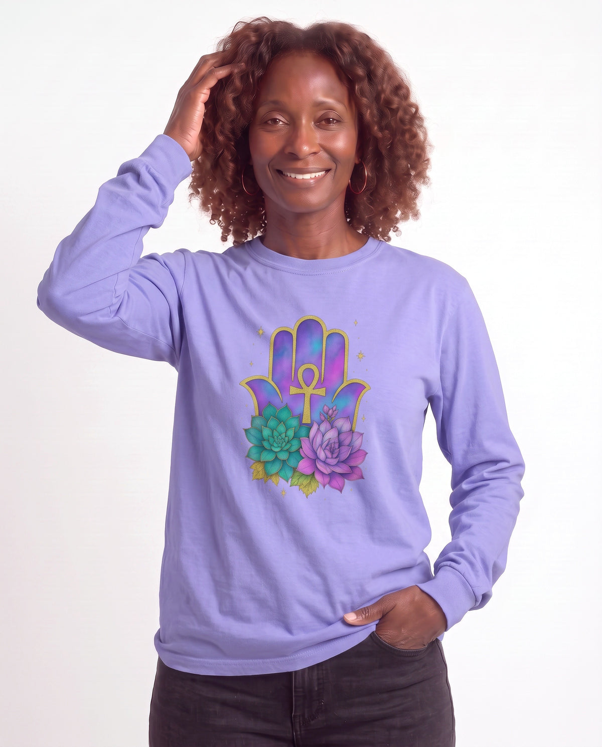 Grace, a Black woman in her 50s with shoulder-length auburn curls and gold hoops, wearing the Hamsa Ankh Bloom Long Sleeve Crewneck Tee in Lilac with a gold Ankh, Hamsa, and blooming succulents. Hands On 5th St.