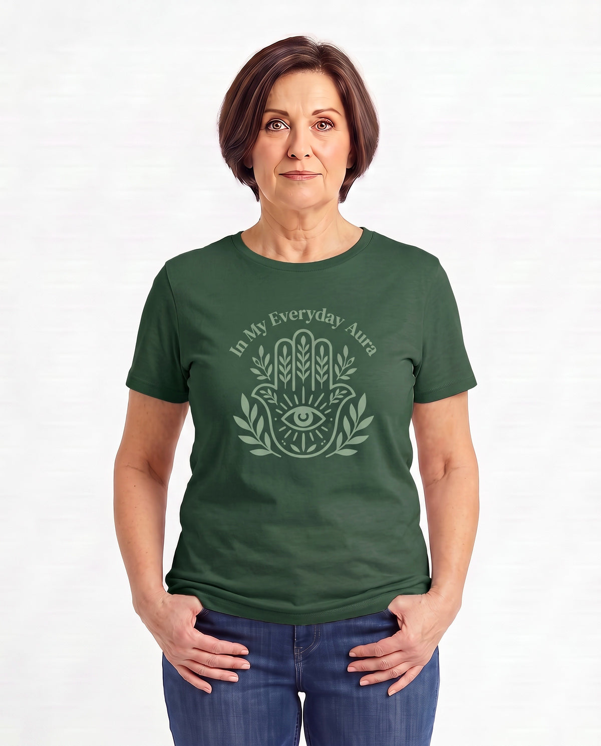 Jillian, a woman in her 50s with a chin-length brown bob, wearing the In My Everyday Aura Signature Tee in Forest Green with an embellished Hamsa. Hands On 5th St.